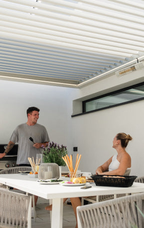 Pergolux Pergola in Weiß mit Outdoor-Küche und zwei Personen beim Grillen.