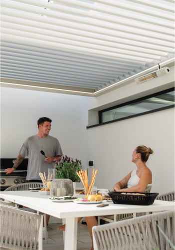 Pergolux Pergola in Weiß mit Outdoor-Küche und zwei Personen beim Grillen.