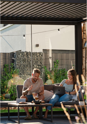 Zwei Personen sitzen unter einer Pergolux Pergola, arbeiten am Laptop und genießen den sonnigen Tag.