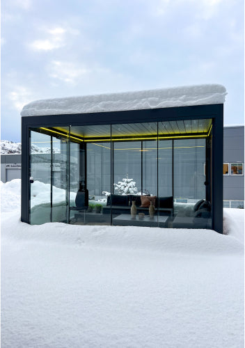 Pergolux Pergola mit Glaswänden im Winter, bedeckt mit Schnee und beleuchtetem Innenraum.