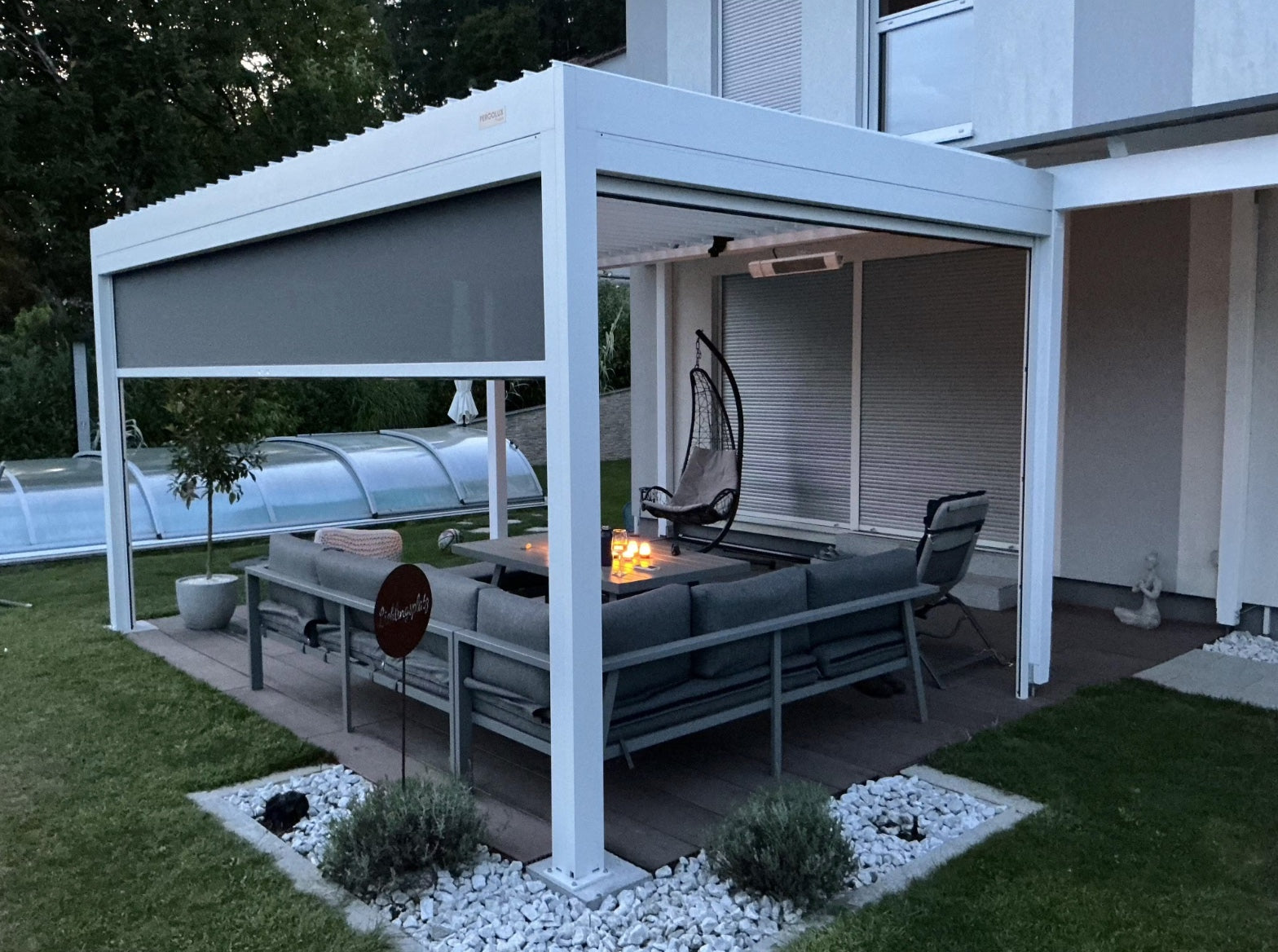 Pergolux Pergola mit LED-Beleuchtung an einem Haus, aufgenommen bei Dämmerung.
