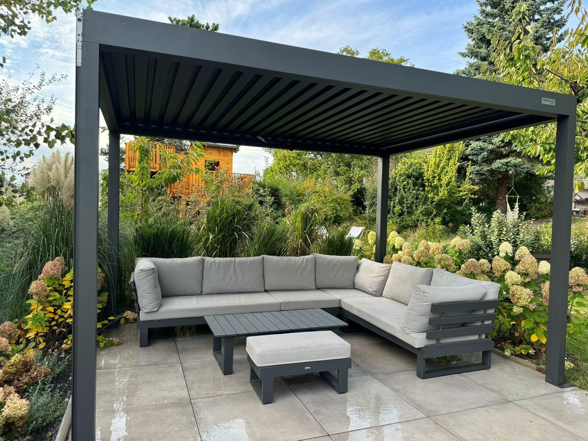 Pergolux Pergola mit Lounge-Möbeln auf Terrasse im grünen Garten.